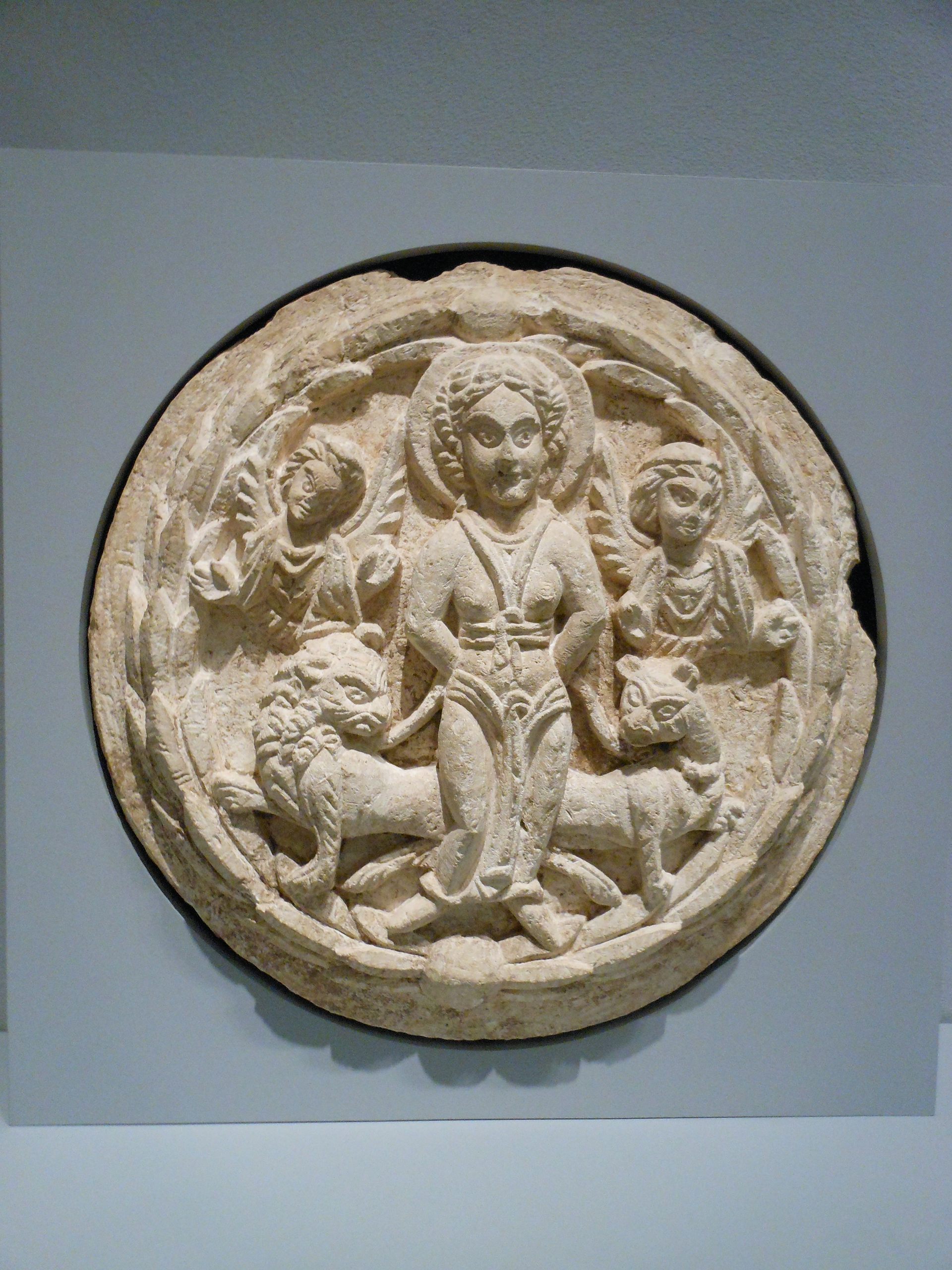 A circular stone with carvings of a bound woman flanked by two lions.
