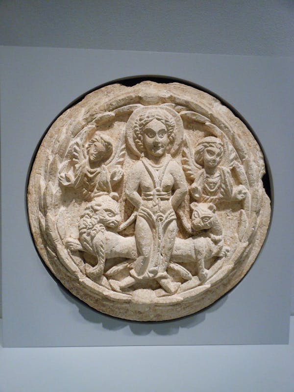 A circular stone with carvings of a bound woman flanked by two lions.