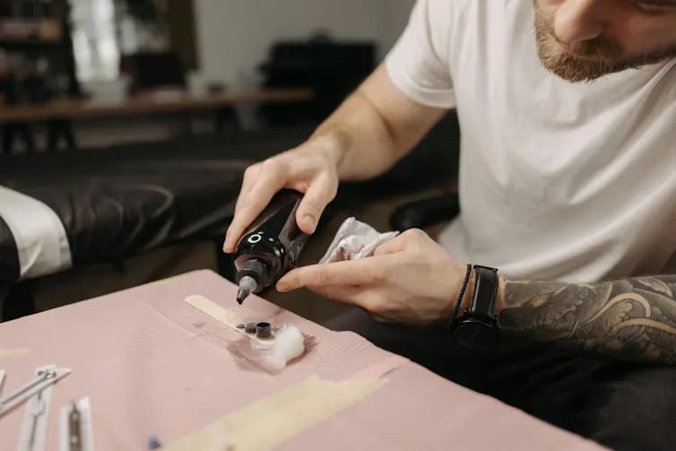 Tattoo artist pouring black ink from a large bottle into small containers.