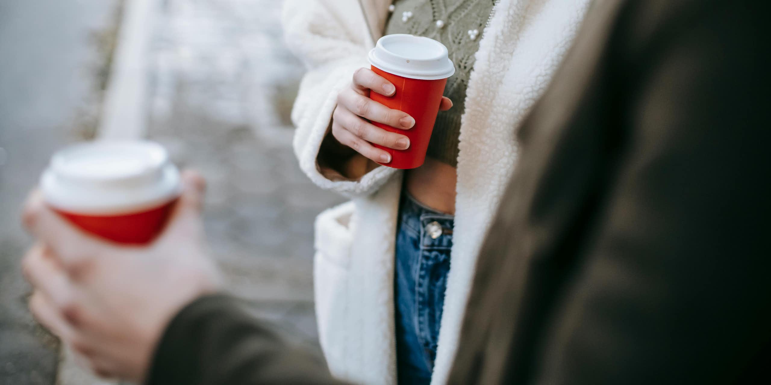 A person holding a red takeaway coffee cup.