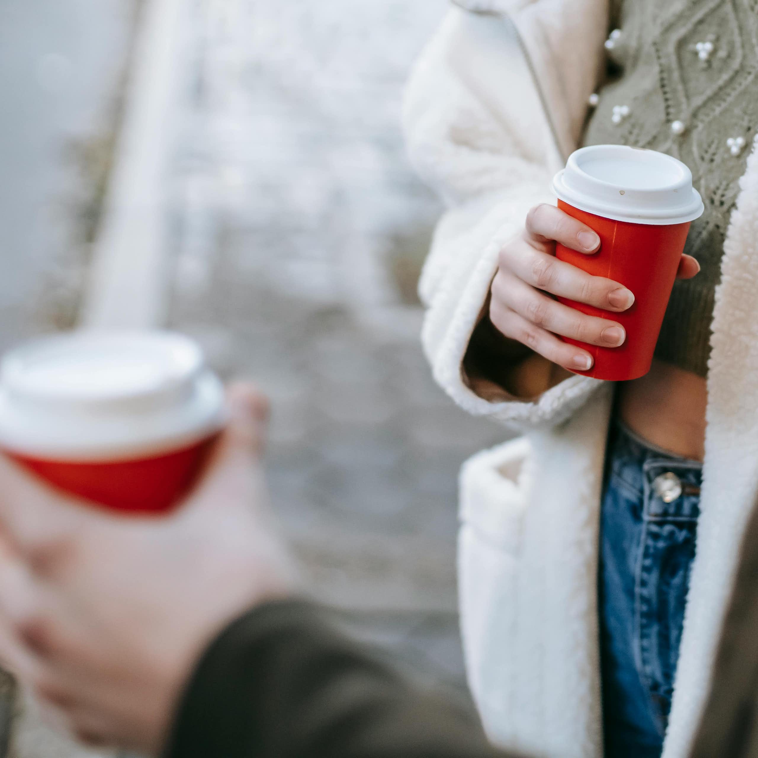 A person holding a red takeaway coffee cup.