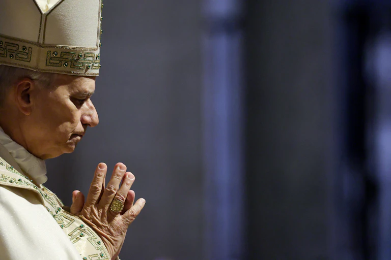 A priest in robes with hands clasped in prayer.