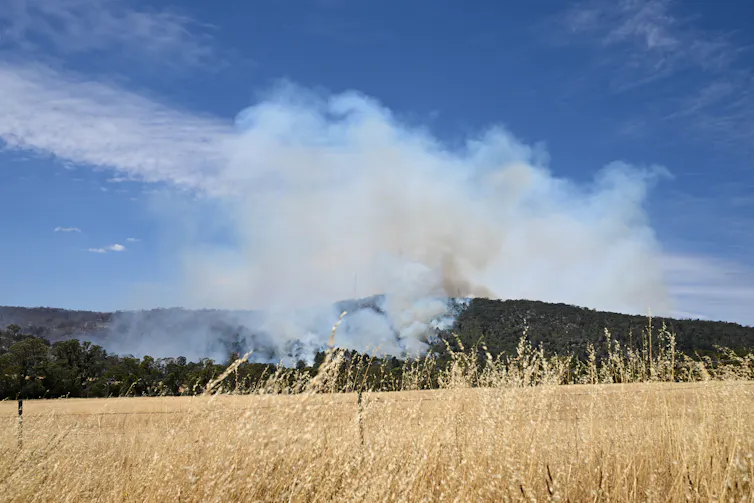 Smoke rises above dark green hills.