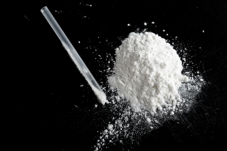 A pile of white powder, possibly ketamine, with a clear plastic straw sitting to the left of it.