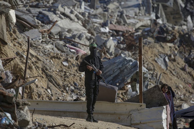 A Hamas fighter stands guard amid the rubble of destroyed buildings.