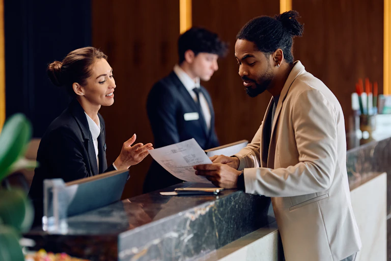 female hotel receptionist smiling and helping a male guest at reception desk.