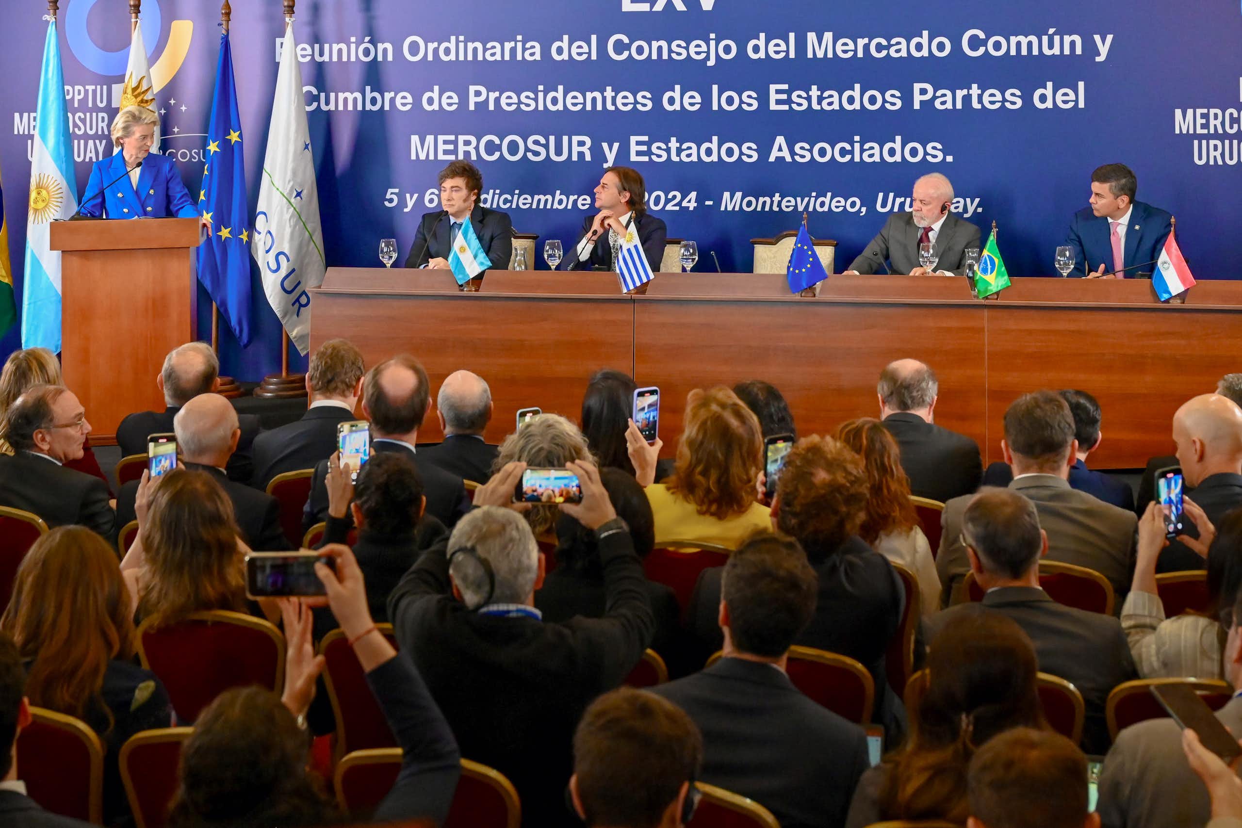 Ursula von der Leyen speaks from a lectern while Javier Milei, Luis Lacalle Pou, Luiz Inácio Lula da Silva and Santiago Peña are seated in a long table next to her