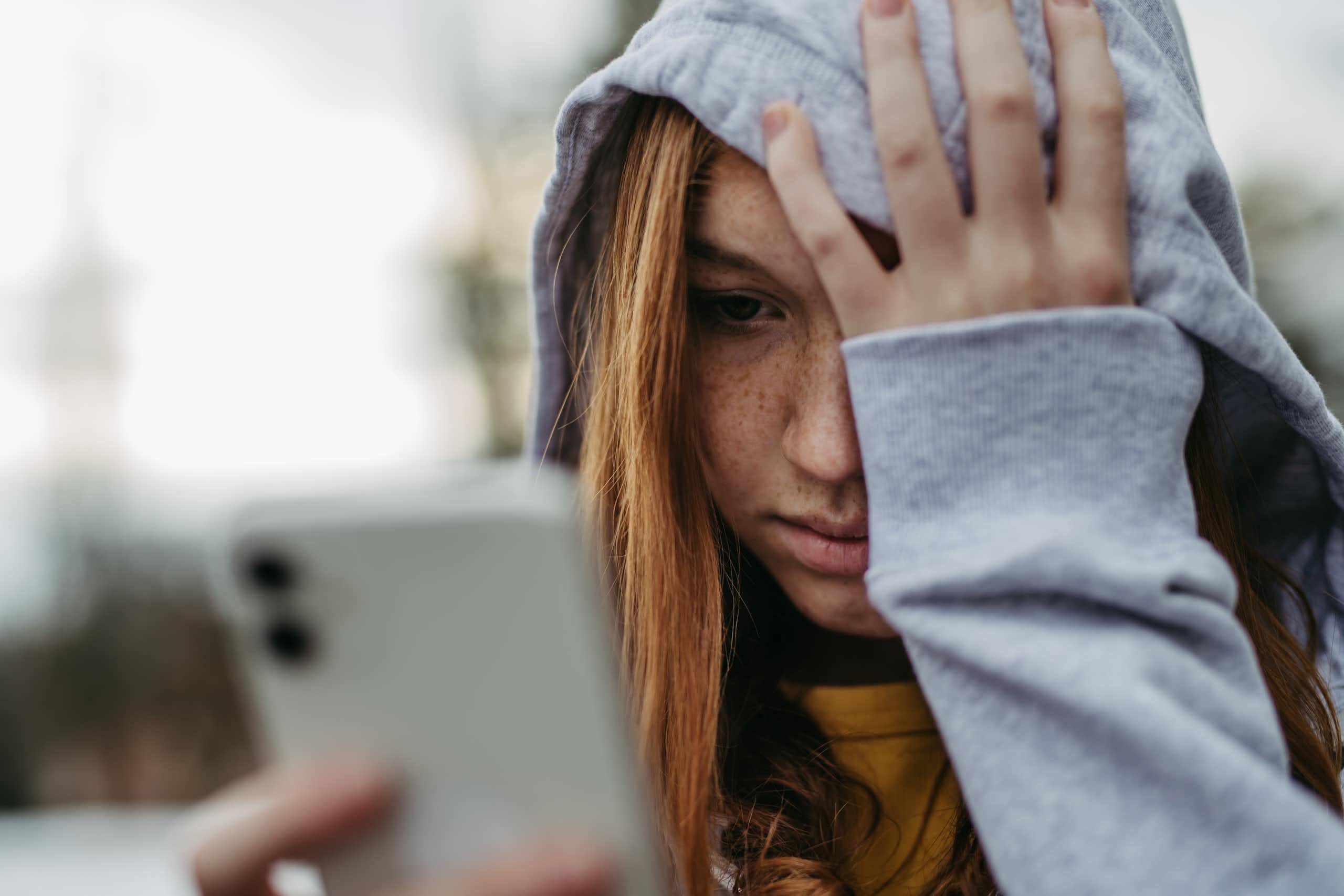 A teen looks at her phone while holding her head in despair.
