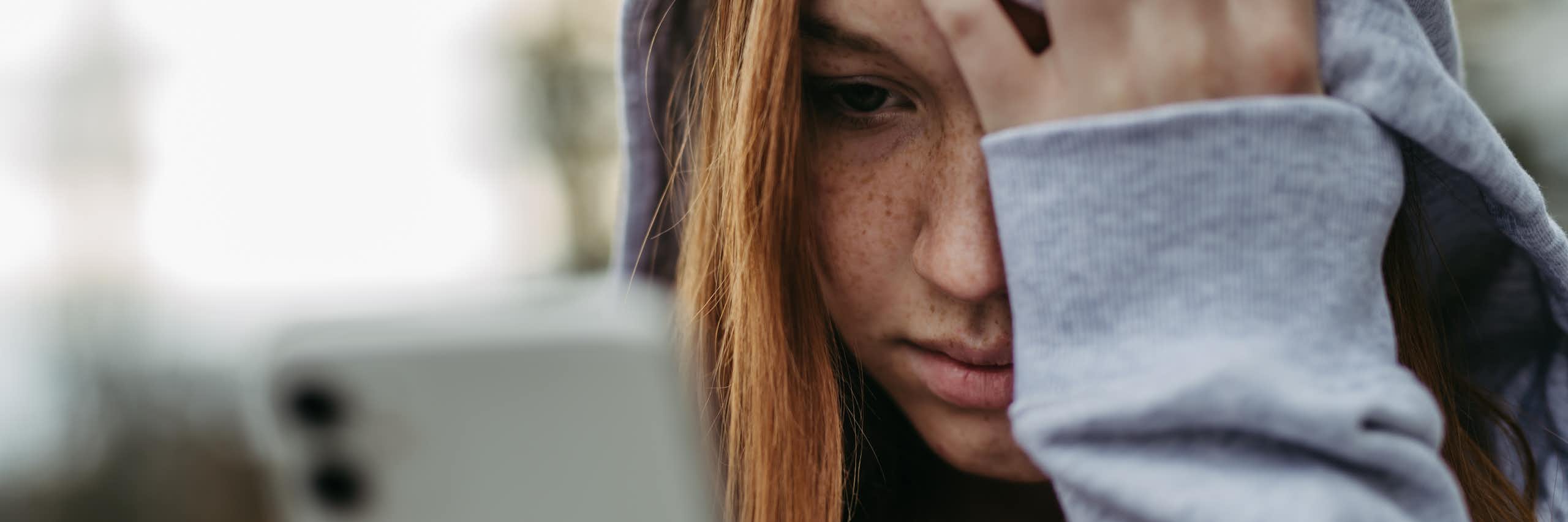 A teen looks at her phone while holding her head in despair.