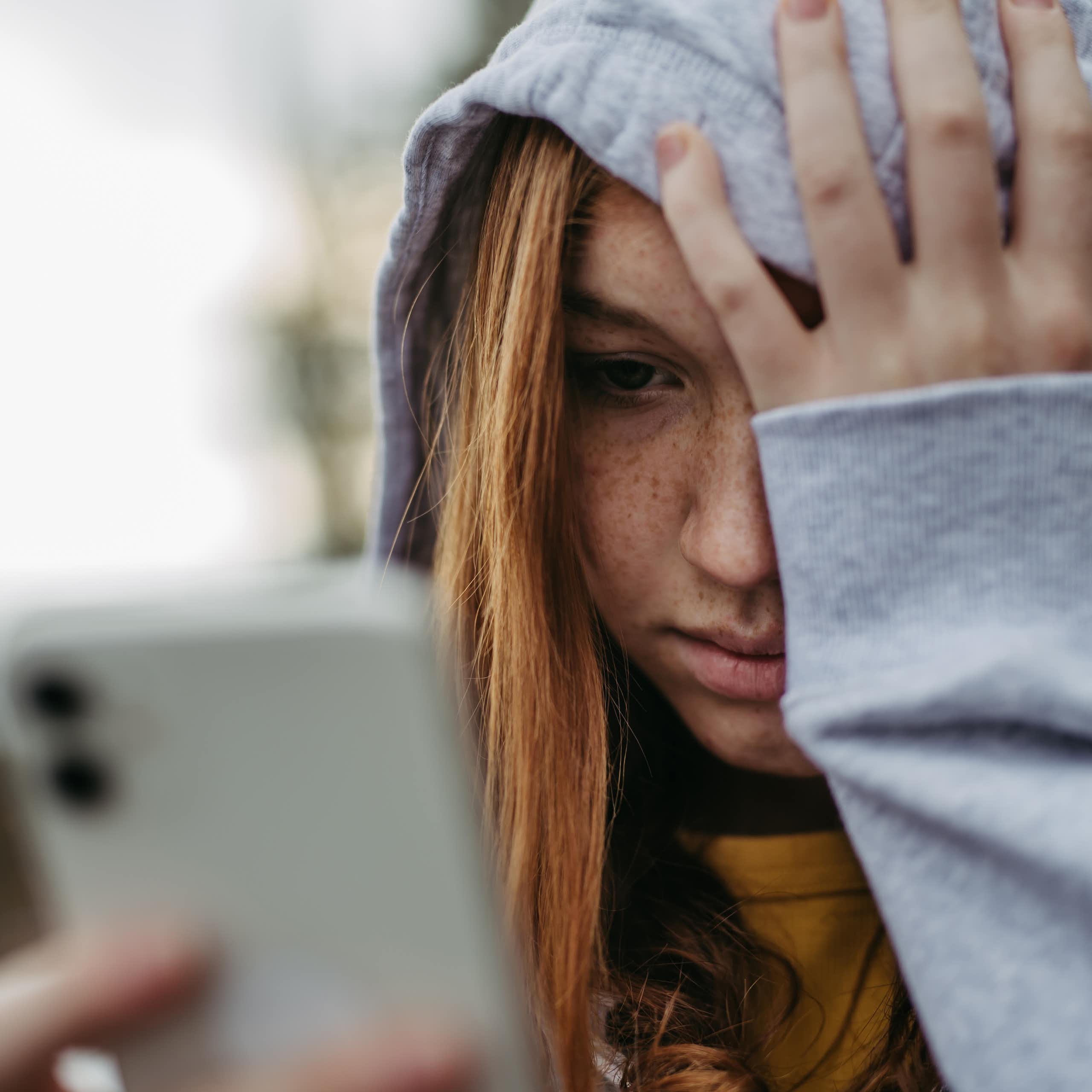 A teen looks at her phone while holding her head in despair.