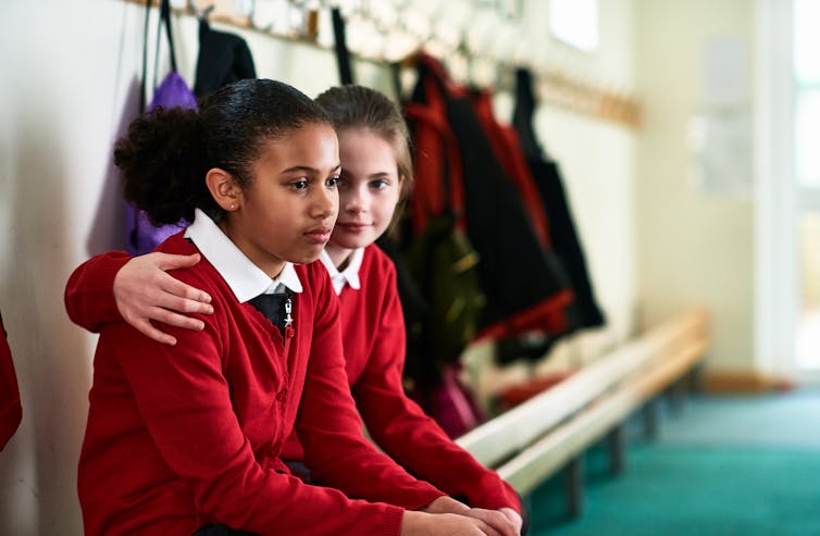 Two girls sitting on a bench at school, one reassuring the other,