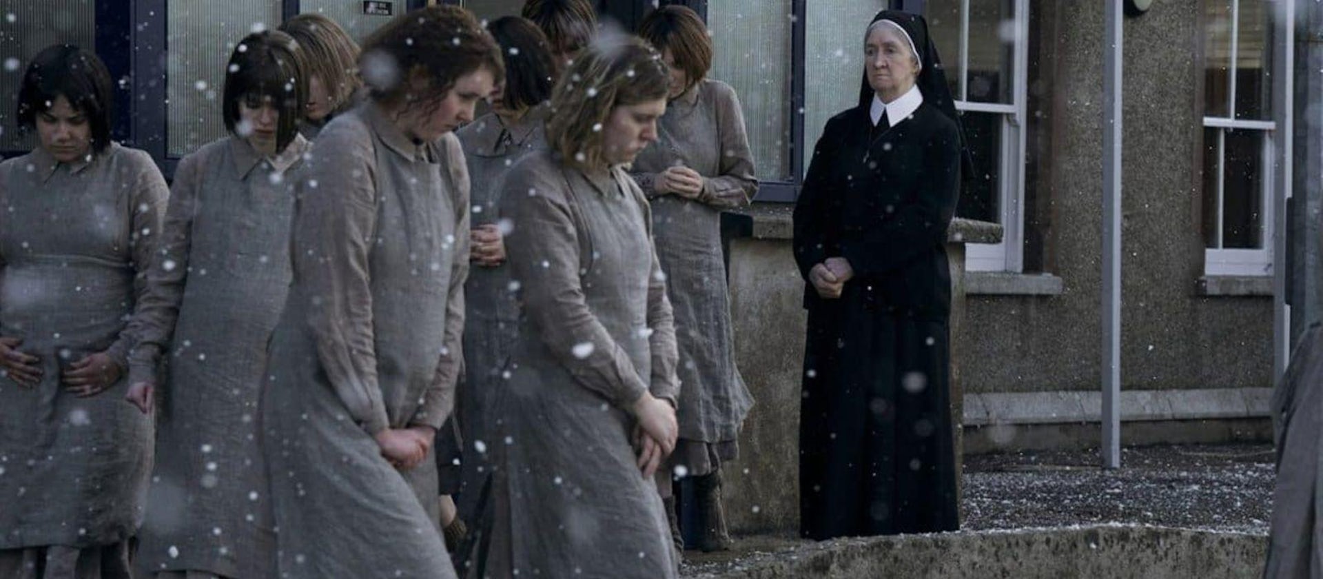Unas jóvenes caminan bajo la nieve ante la mirada de una monja.