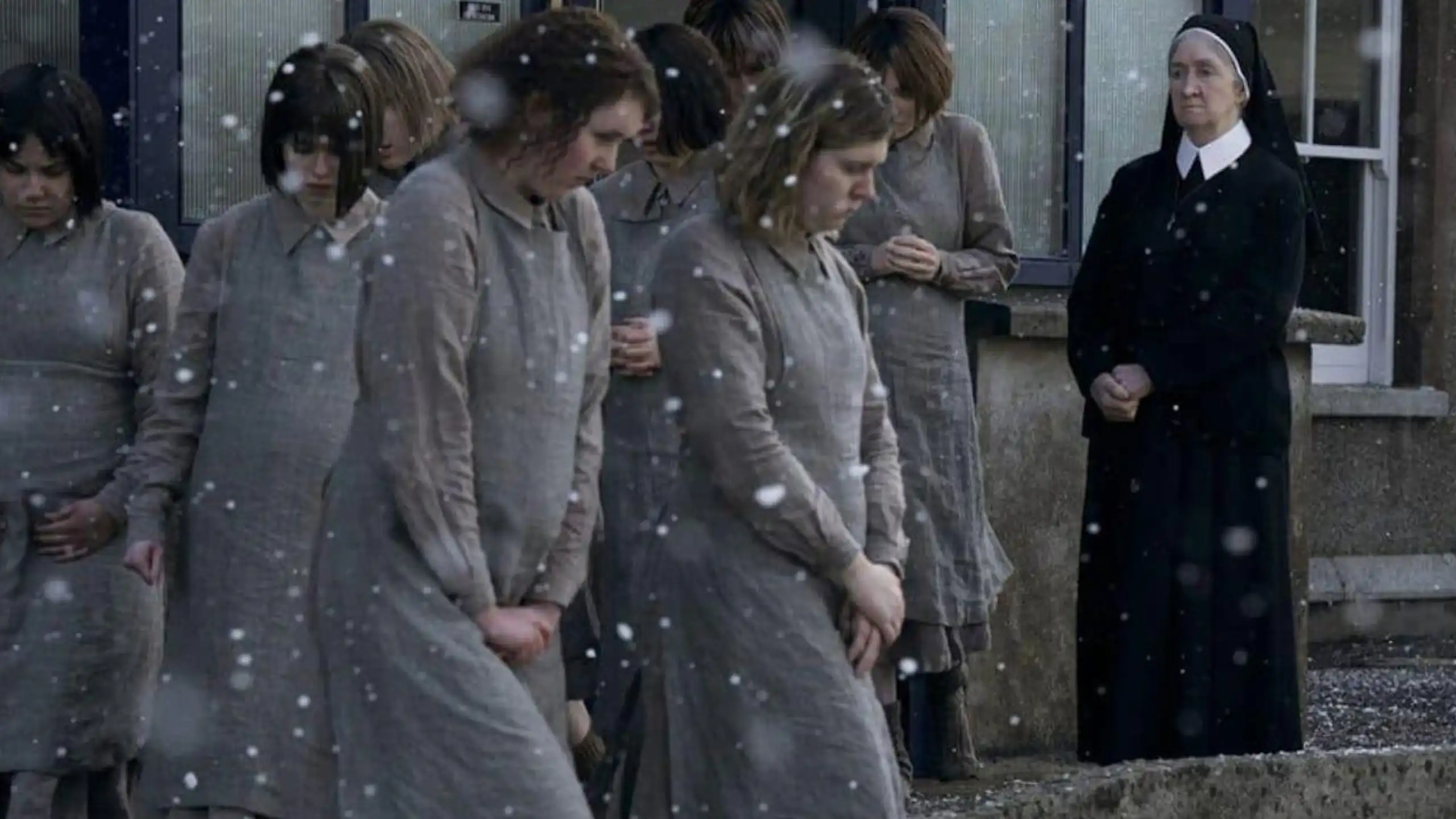 Unas jóvenes caminan bajo la nieve ante la mirada de una monja.