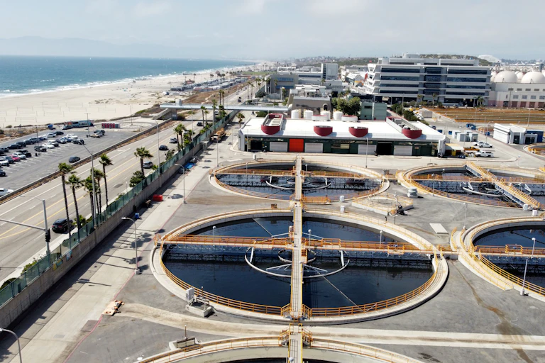 A group of circular industrial ponds stand next to an oceanside beach.