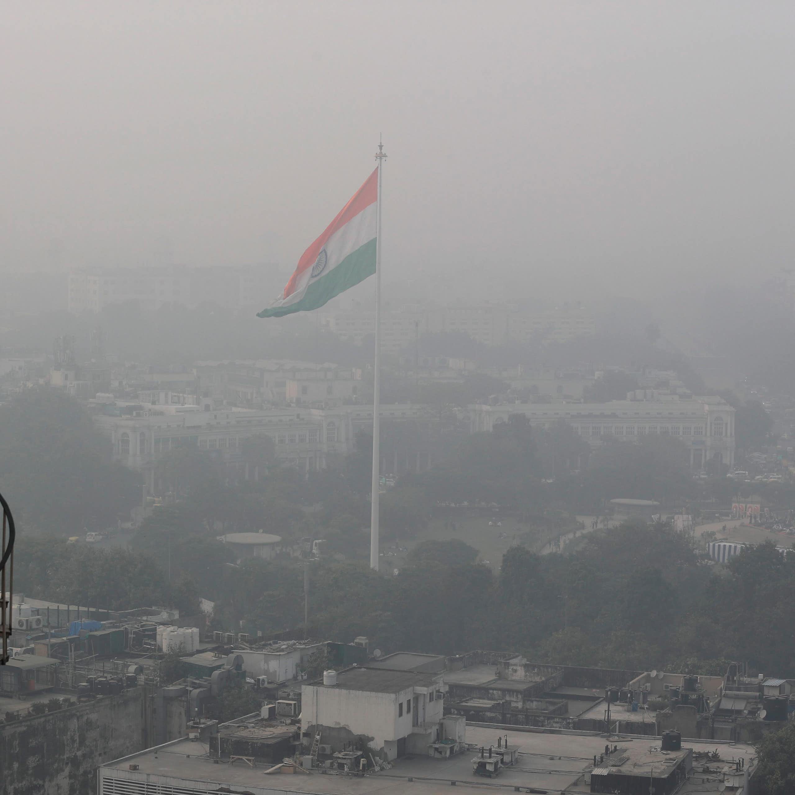 a large indian flag flies on a pole above a city enveloped in smog