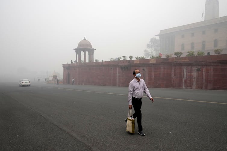 un hombre con una máscara en la cara camina por una calle con una espesa niebla tóxica