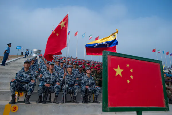 Men in army fatigues sit behind two flags.