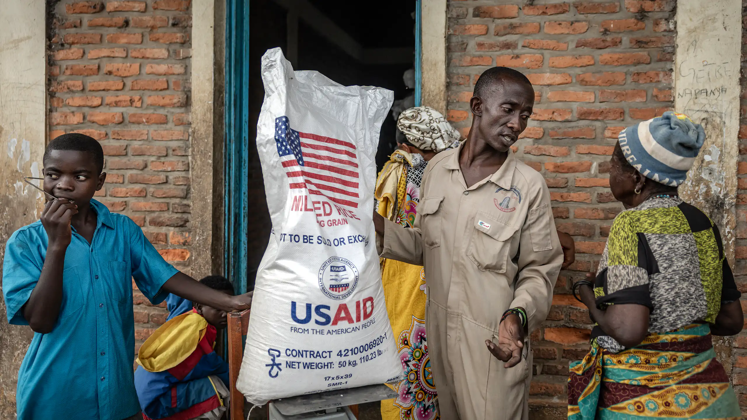 A man holds a sack of rice with USAID branding on it while speaking to other people.