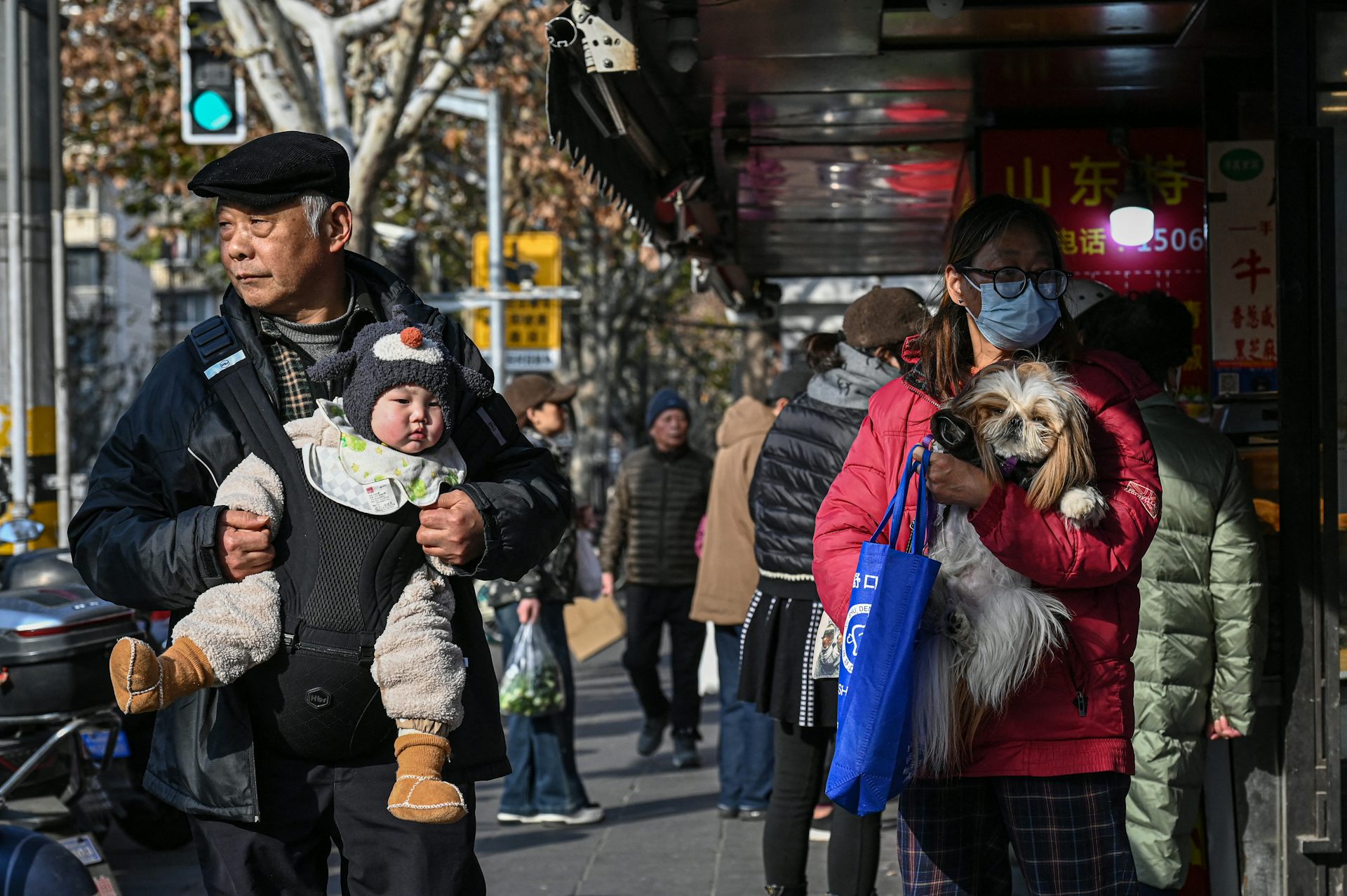 A man holds a baby while a woman carries a dog.