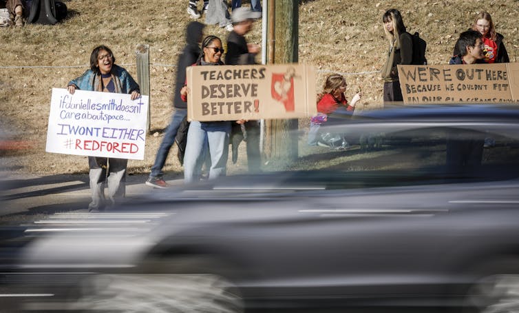 Los coches pasan junto a estudiantes con carteles de protesta en apoyo a sus profesores en huelga