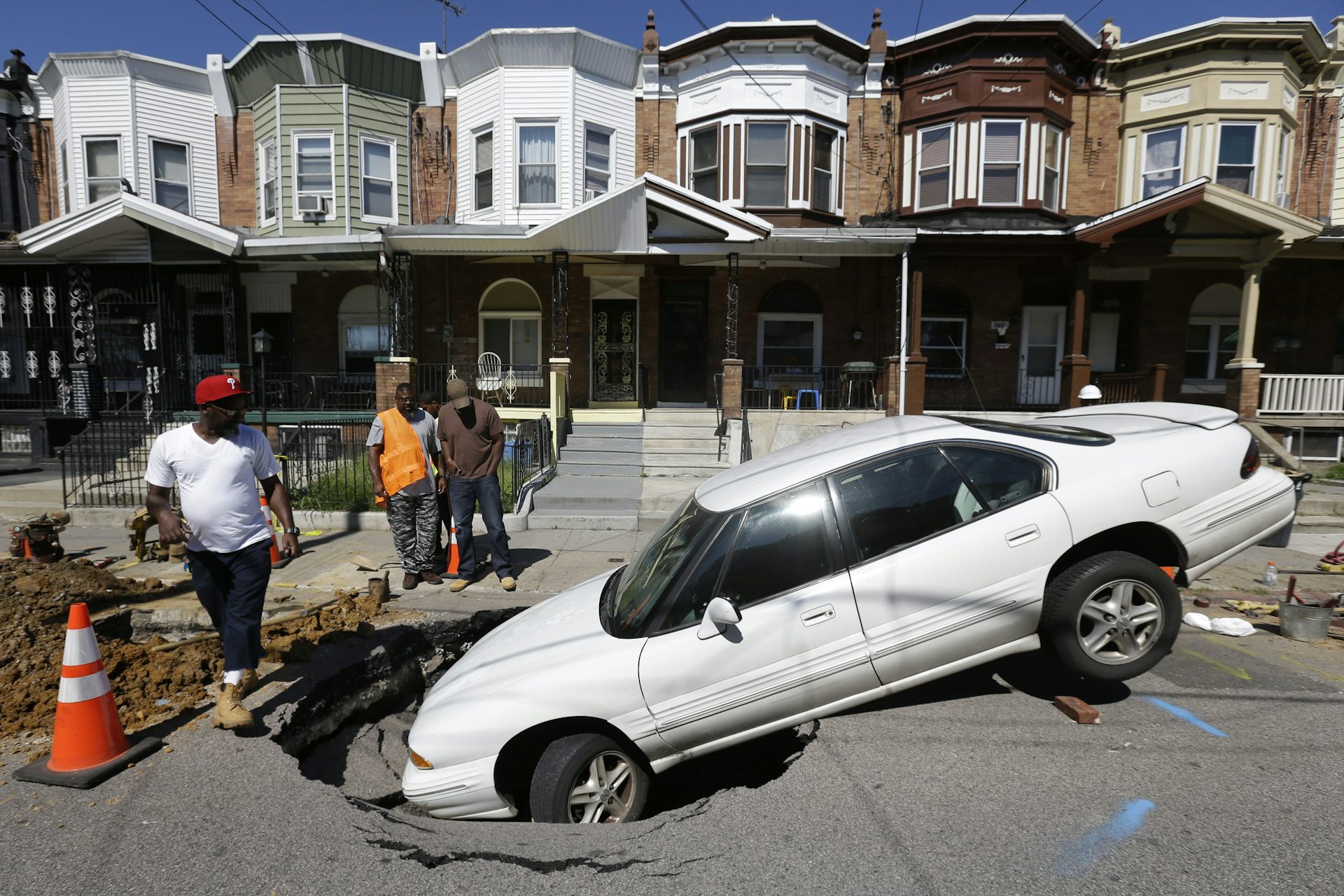 Front half of white sedan in a sinkhole on residential street