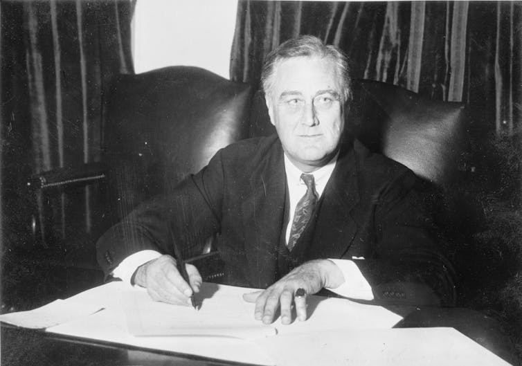 A black and white photo of Franklin D Roosevelt signing documents.