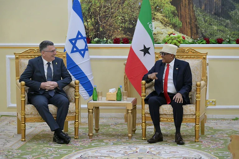Two men talking to each other while seated, with flags behind them