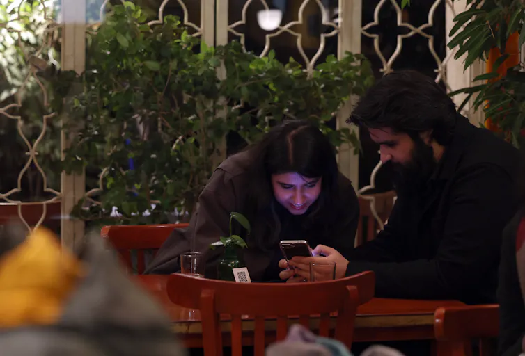 Two young Iranian people on their phones in an internet cafe