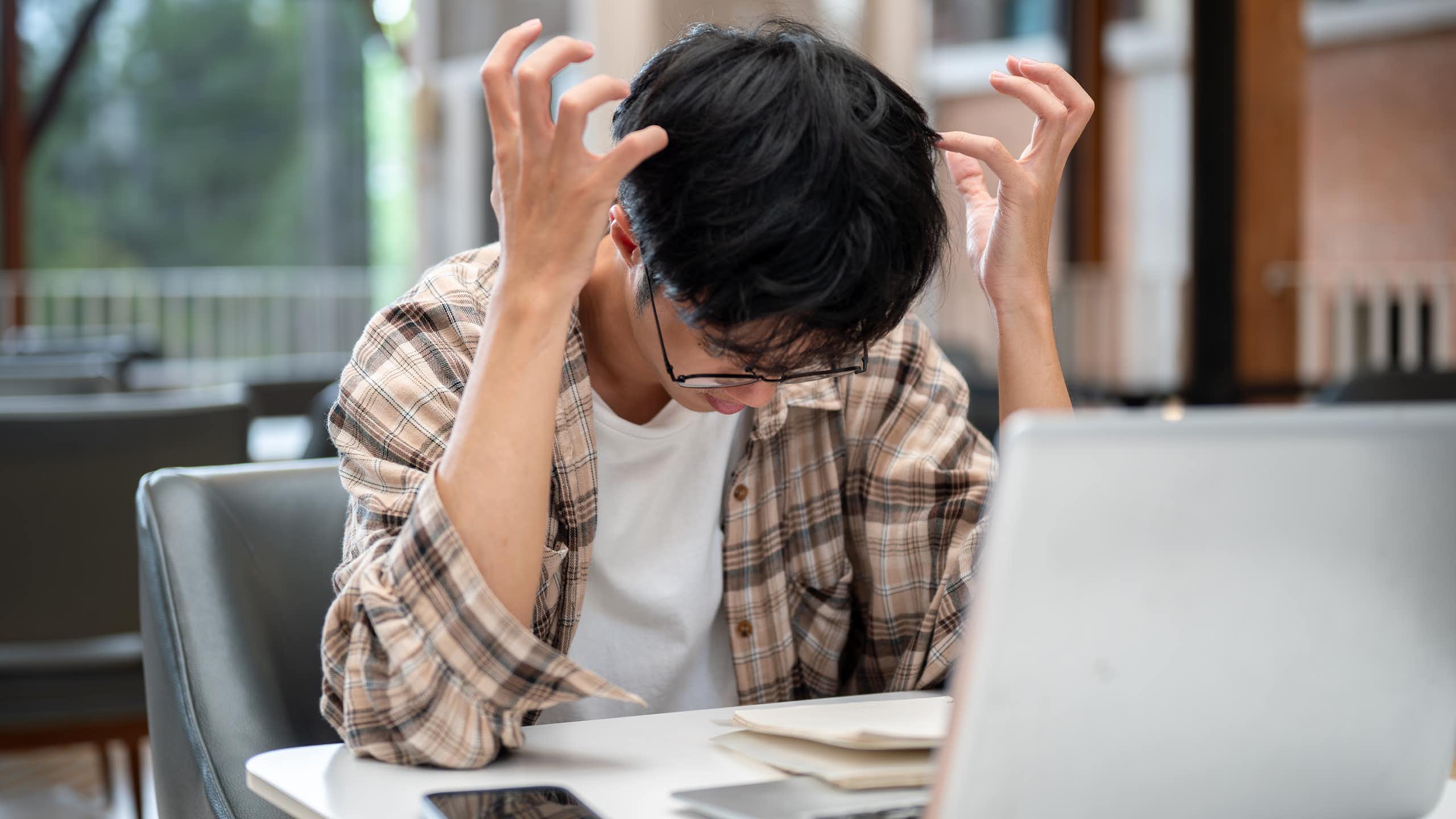 Un chico hace gestos de desesperación ante un ordenador portátil