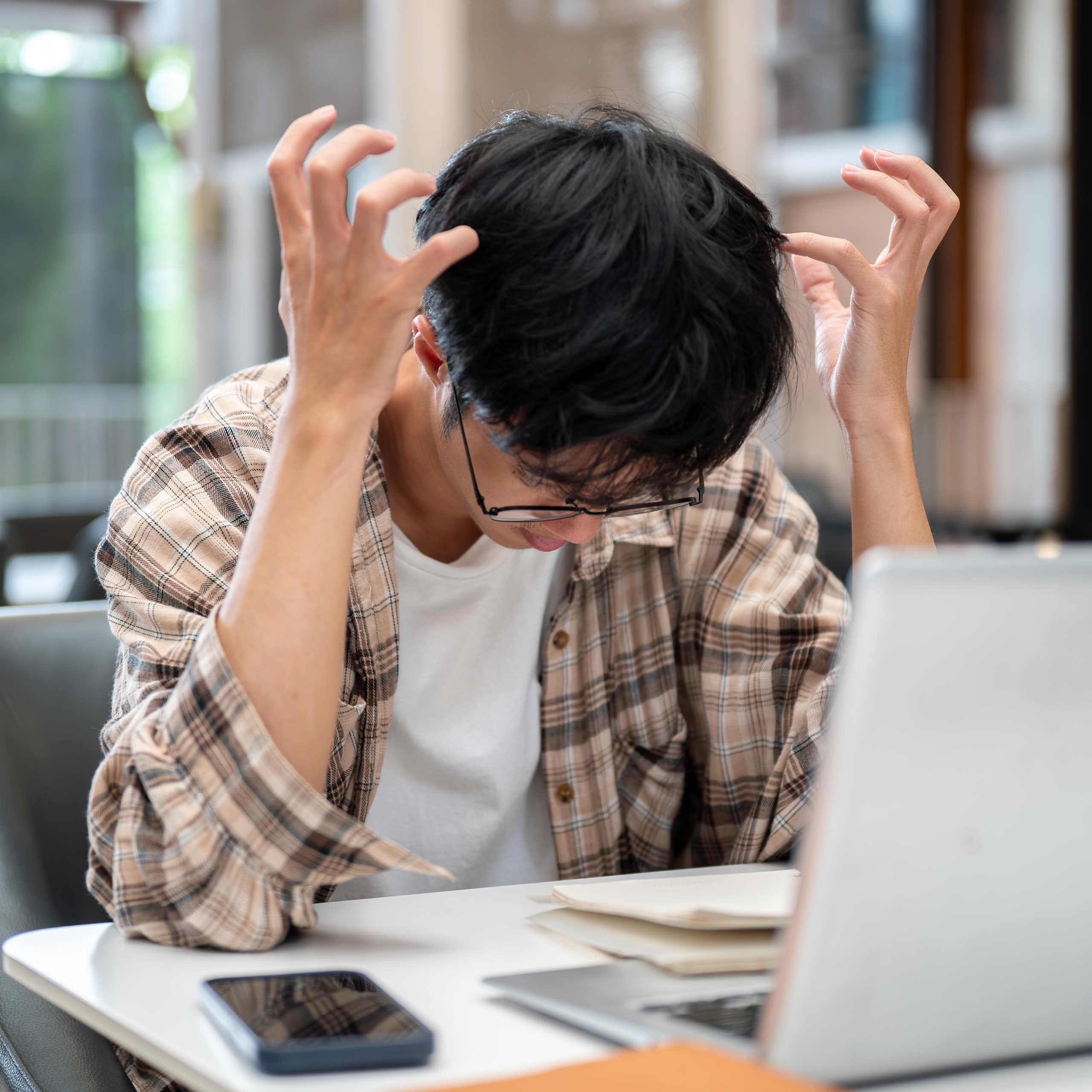 Un chico hace gestos de desesperación ante un ordenador portátil