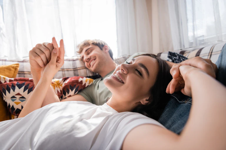 Blurred man holding hands of happy girlfriend on bed in camper van See less