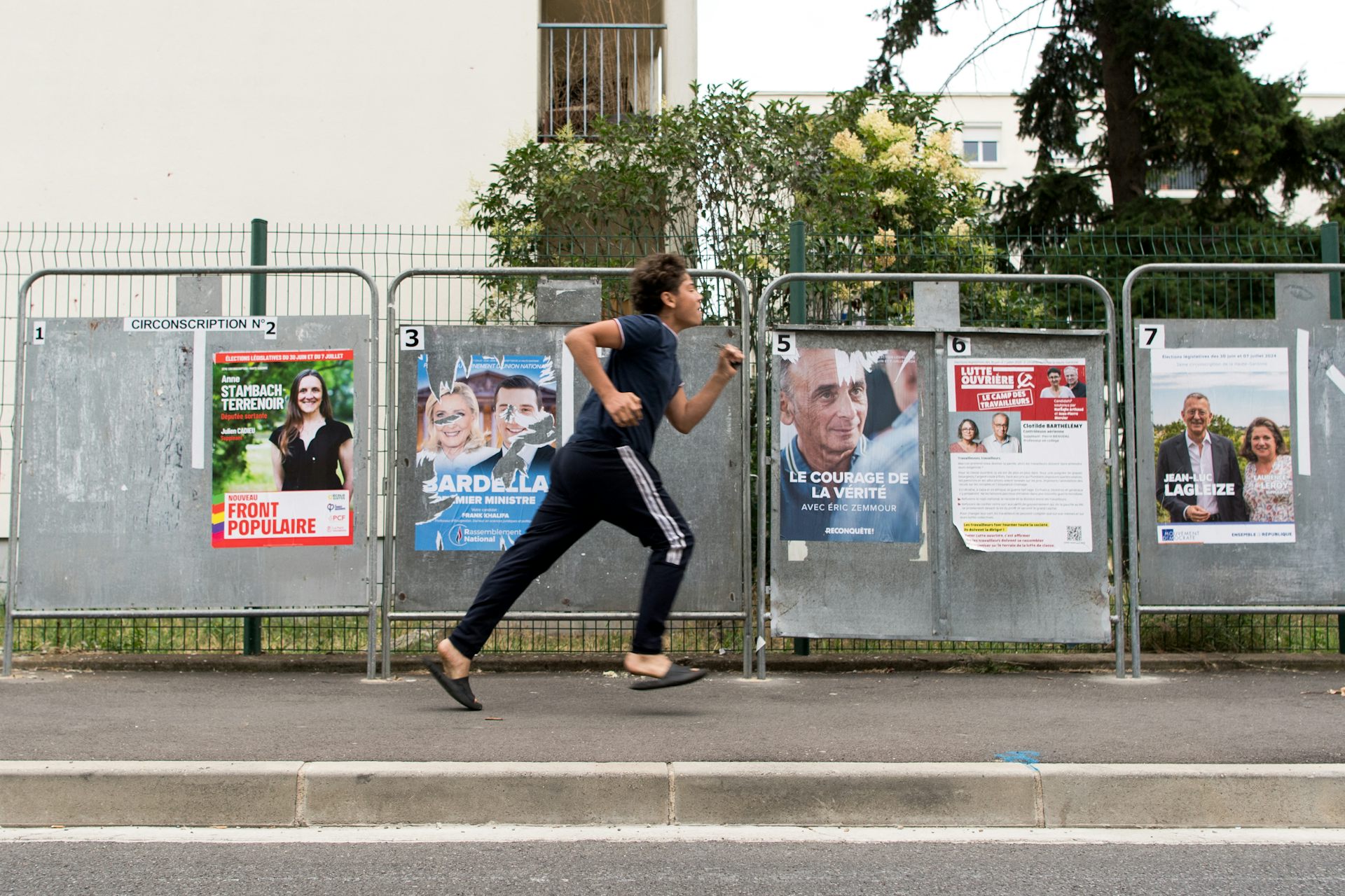 Un jeune homme passe en courant devant des panneaux d'affichage électoral, dans le quartier populaire des Izards, à Toulouse, en juillet 2024