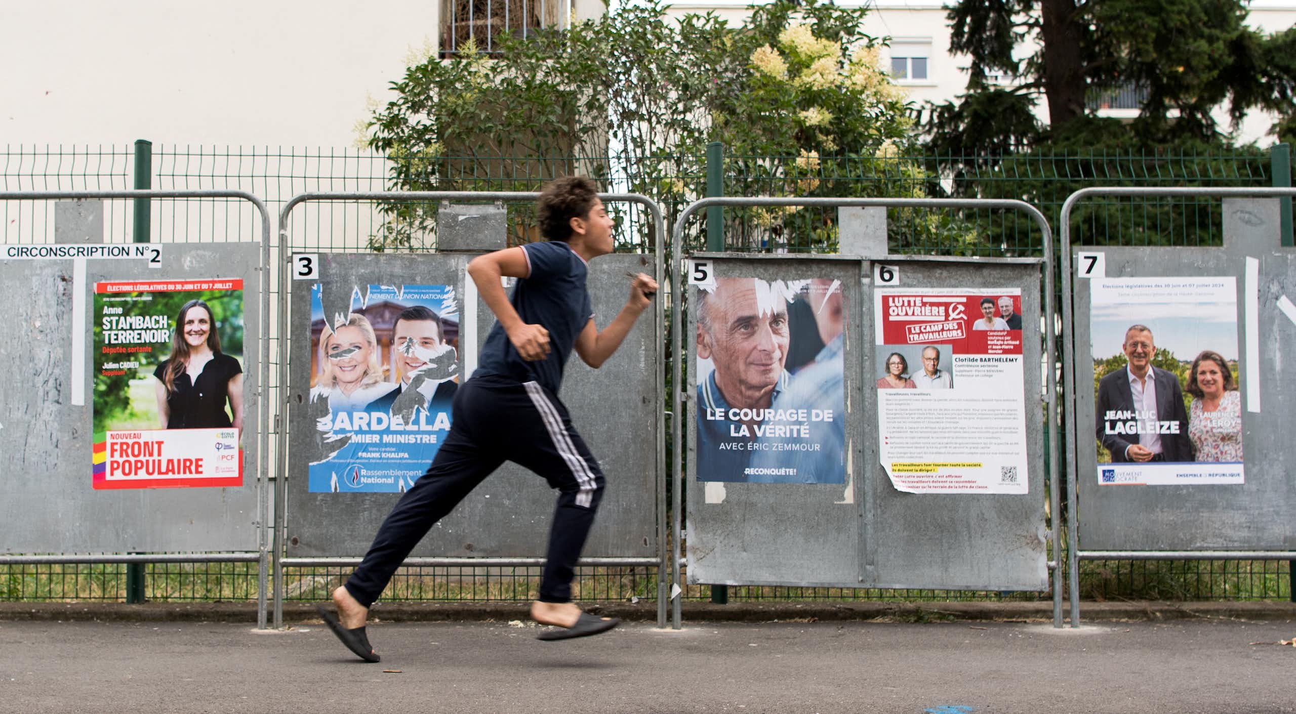 Un jeune homme passe en courant devant des panneaux d'affichage électoral, dans le quartier populaire des Izards, à Toulouse, en juillet 2024