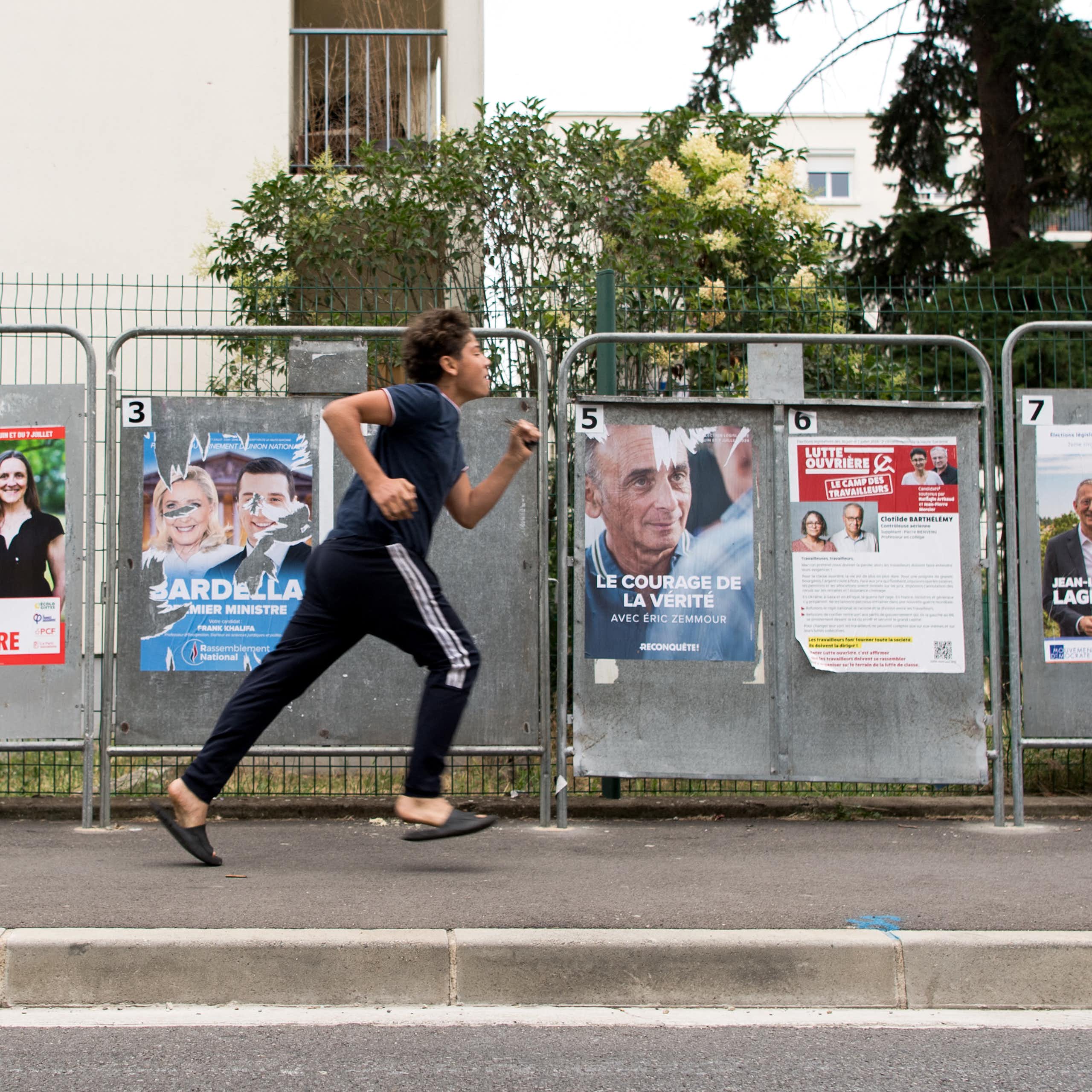 Un jeune homme passe en courant devant des panneaux d'affichage électoral, dans le quartier populaire des Izards, à Toulouse, en juillet 2024