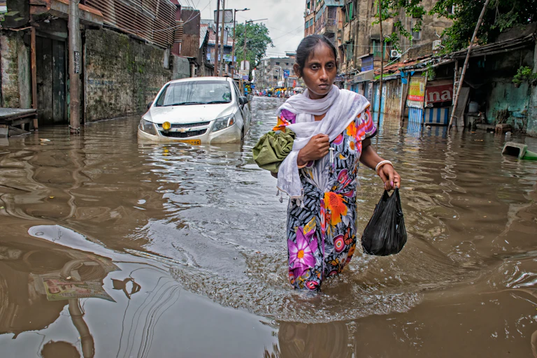 woman wades through flooded street in India holding black bag of belongings