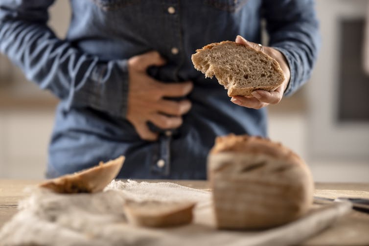 A person holding a slice of bread with one hand and their stomach with the other.