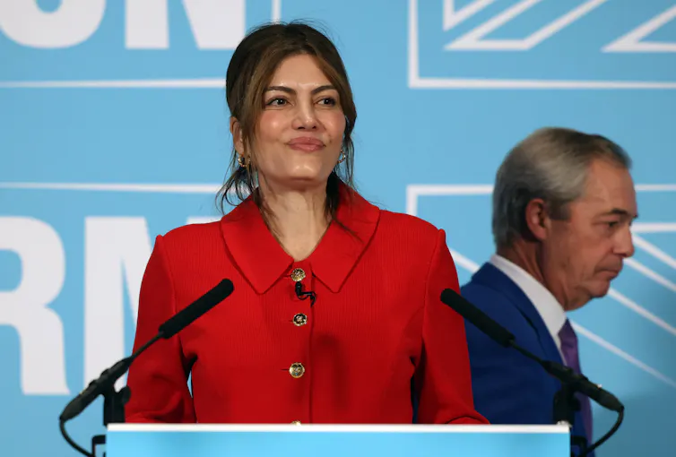 Laila Cunningham, dressed in a red jacket, speaks at a podium in front of a Reform blue background