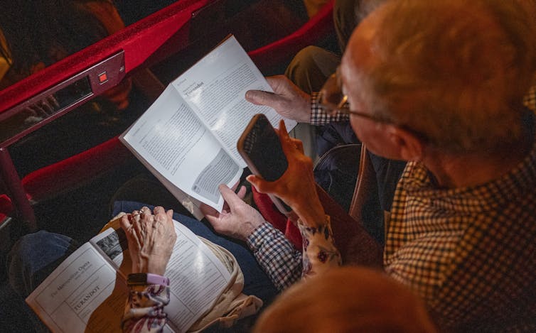 A couple reads program notes in a theater.