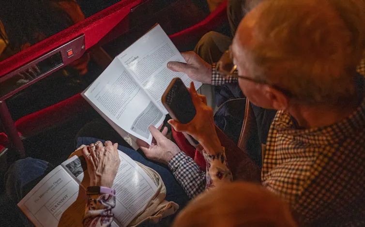 A couple reads program notes in a theater.