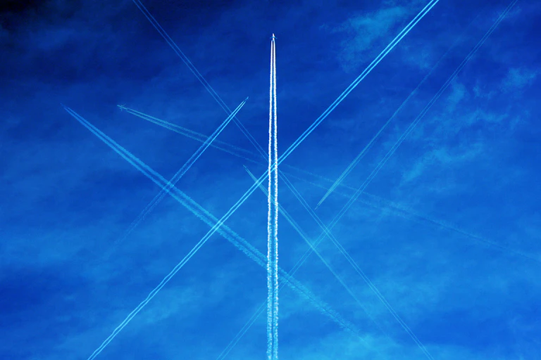 Airplanes leave trails in a bright blue sky.