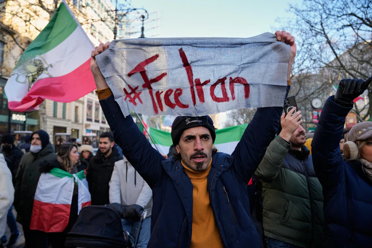 A group of protesters walking down the street and carrying flags and signage that reads Free Iran
