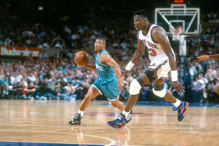 Basketball player running with ball on court, a player twice his height running beside him