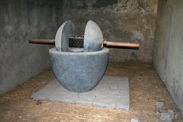 A grey bowl with two grey presses sitting on a wooden dowel.