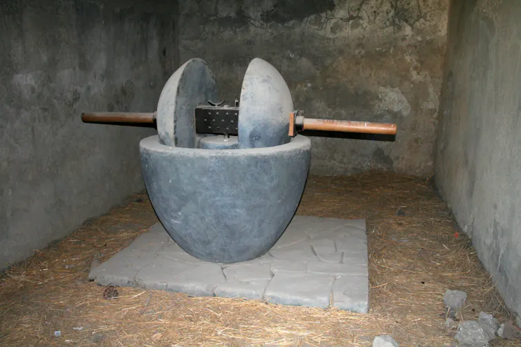 A grey bowl with two grey presses sitting on a wooden dowel.