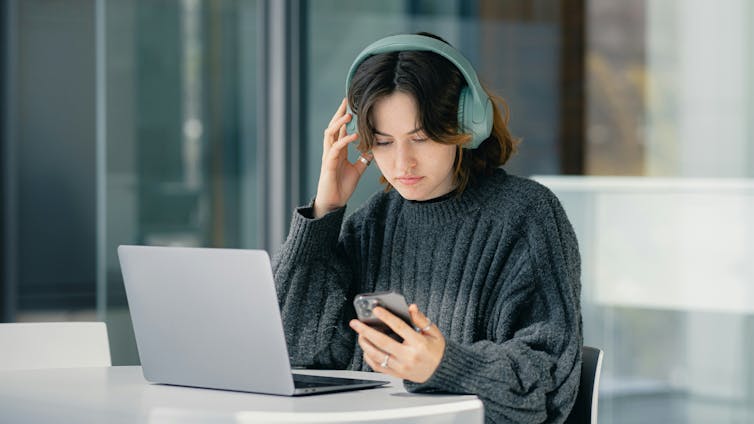 A woman wearing headphones sits at a laptop.