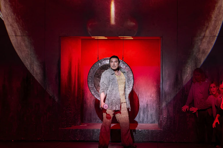 A man sings in front of a giant red mask.