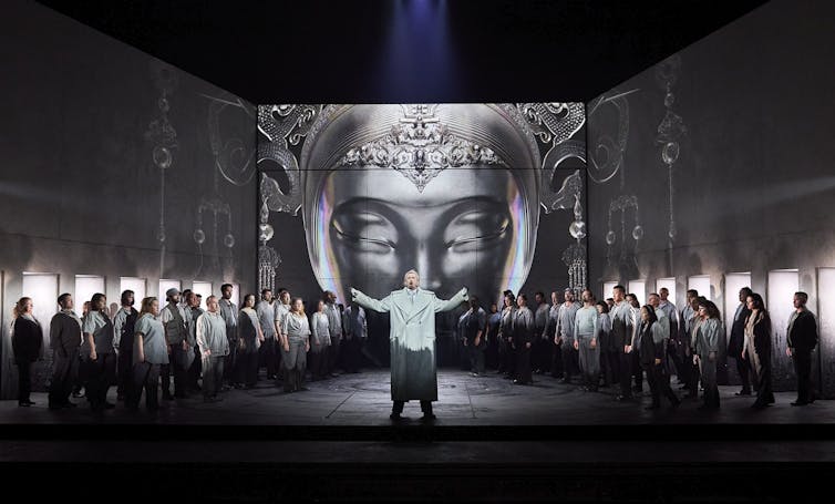The chorus stands in front of the giant mask.