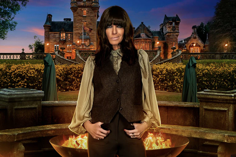 A woman with dark hair standing dramatically in front of a castle, lit by torches.