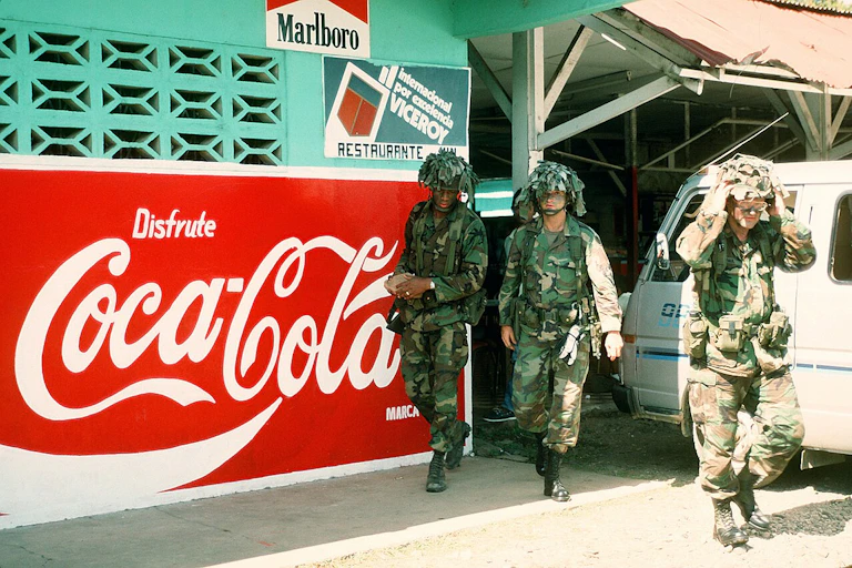 Solados junto a un cartel de Coca-Cola.
