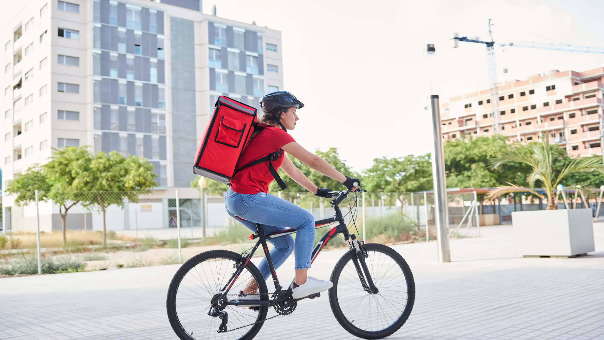 Una repartidora en bici amb la motxilla del repart a l'esquena.